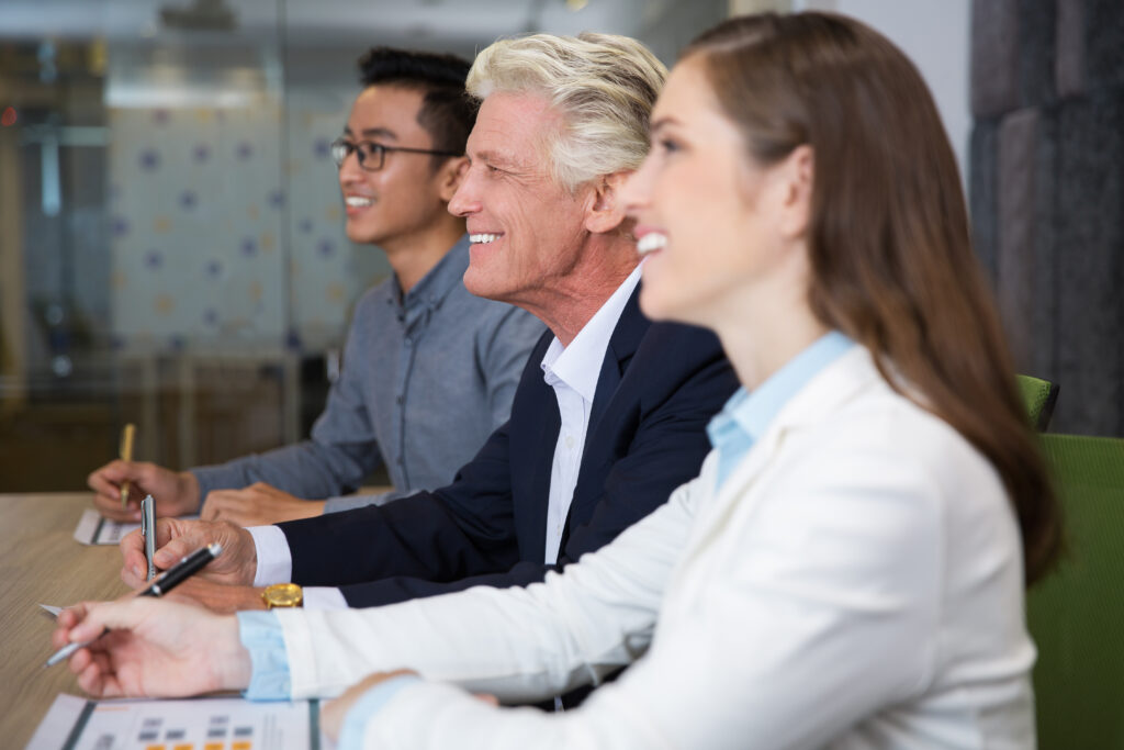 Vista lateral de tres profesionales: dos jóvenes (hombre y mujer, de 20 a 30 años) sonrientes junto a un empresario senior (60 años), simbolizando mentoría, colaboración y el talento senior en startups en un entorno empresarial.